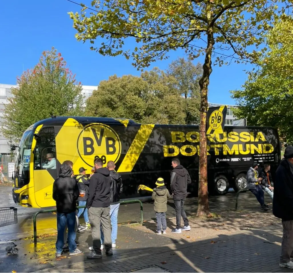 BVB III Schwarzer und gelber Mannschaftsbus von Borussia Dortmund auf einer Straße mit Fans in der Nähe.
