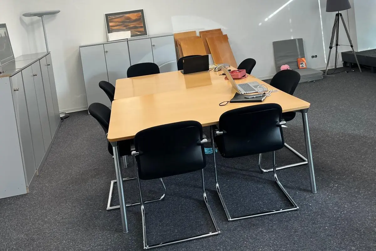 Ein Konferenztisch aus Holz mit mehreren schwarzen Stühlen und einem Laptop auf der Oberfläche in einem Büro.